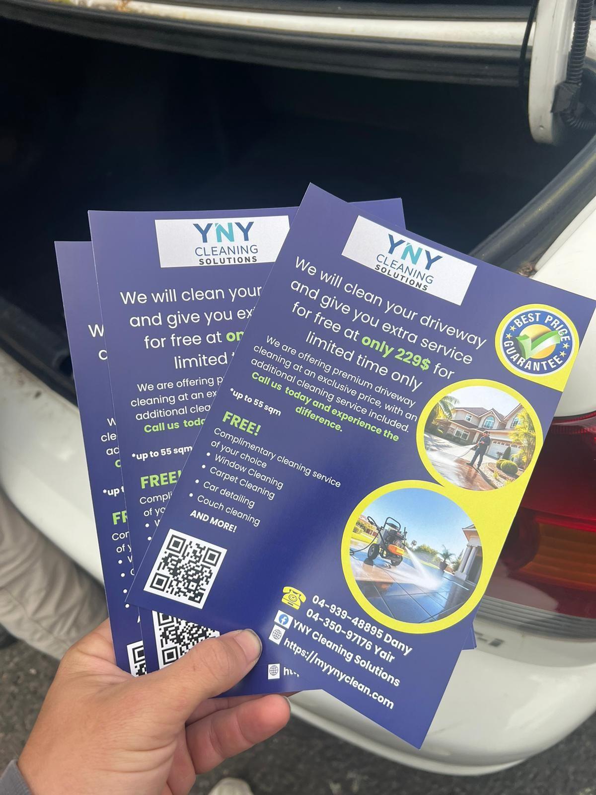 Hand holding YNY Cleaning Solutions flyers near a car trunk, advertising driveway cleaning services and offers.